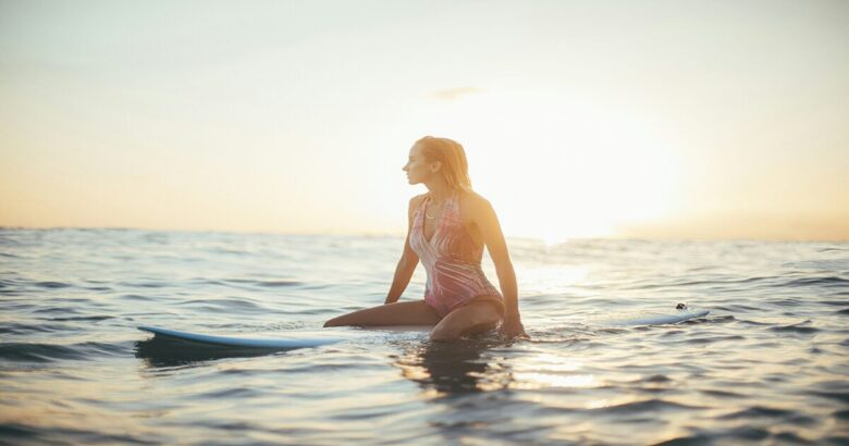 朝焼けの海でサーフボードに乗り波を待っている女性